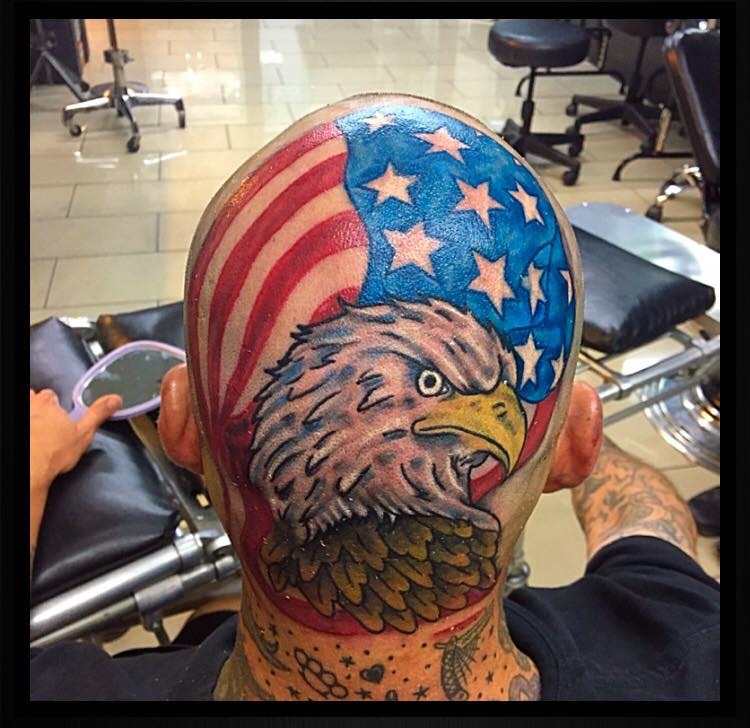 Side-profile of an eagle head in front of an American flag tattooed on the back of a bald man’s head