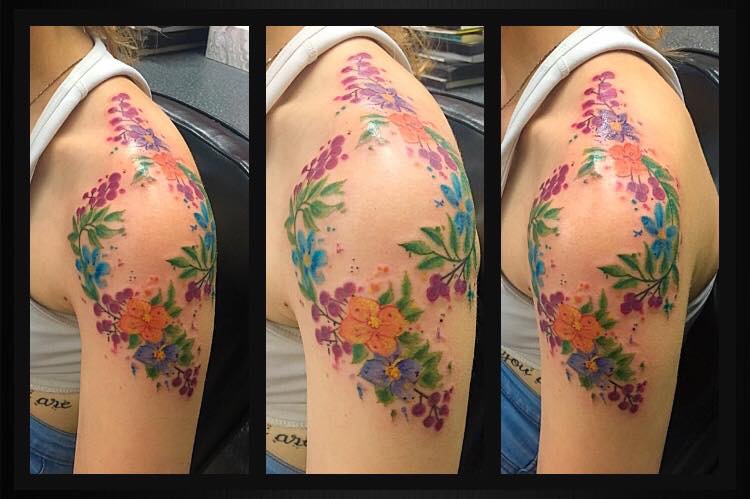Wreath of blossoming flowers tattooed on the shoulder spanning to the bicep